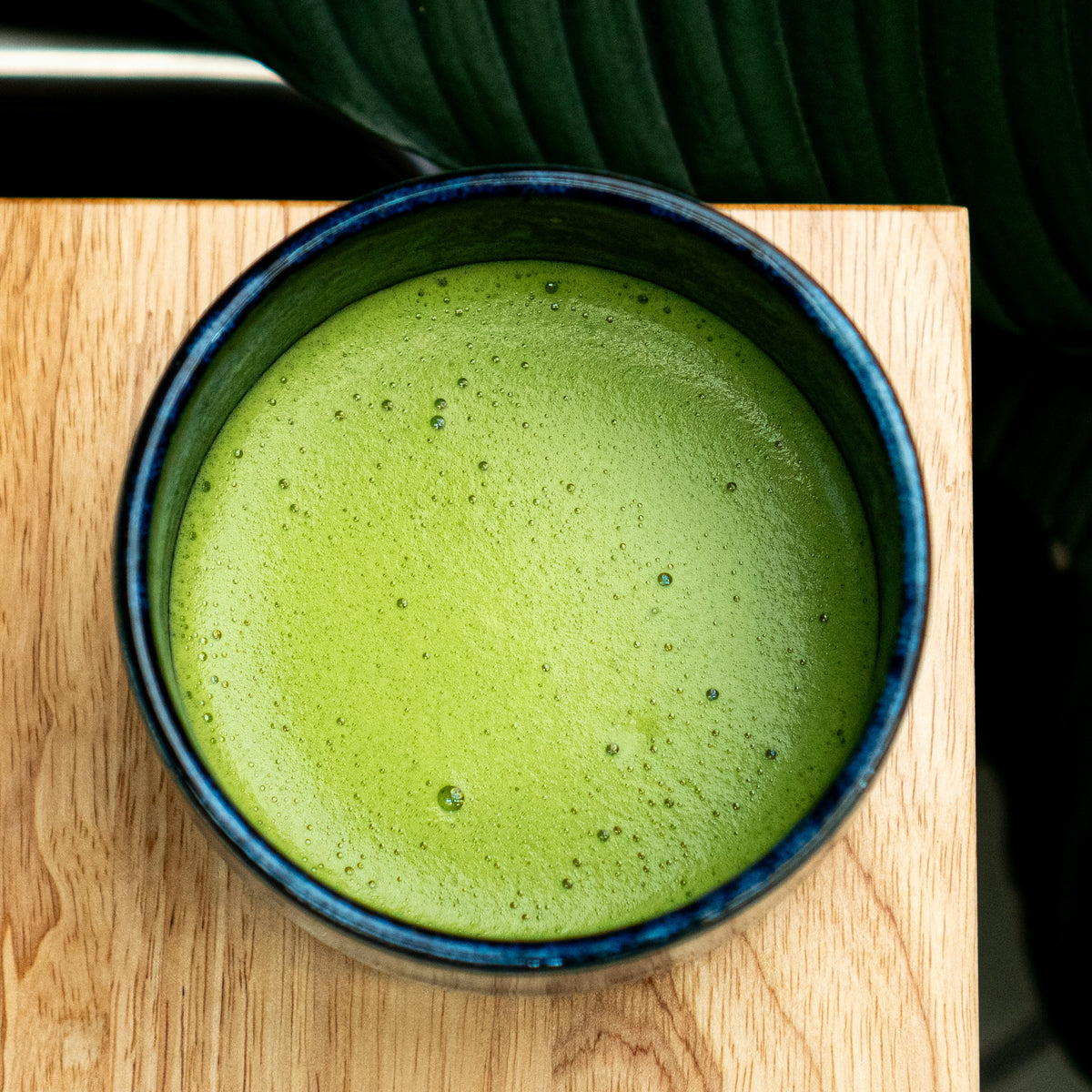 Japanese Organic matcha matcha tea in a blue ceramic bowl on a wooden surface with a leaf in the background
