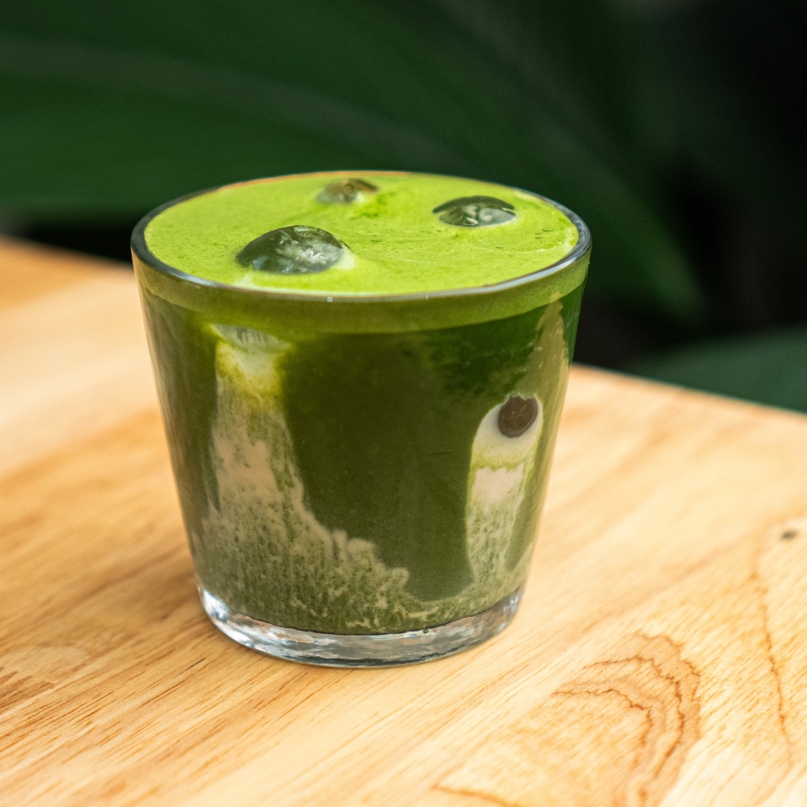 Green tea matcha latte with ice cubes in a glass on a wooden surface
